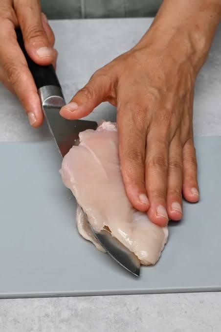 Manos fileteando pechuga de pollo con cuchillo - preparación de milanesas caseras